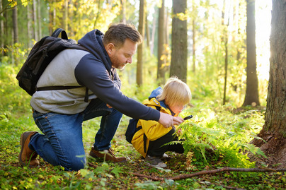 School boy and his father hiking together and exploring nature with magnifying glass. Little boy and dad spend quality family time in sunny forest of second summer. Daddy and little son