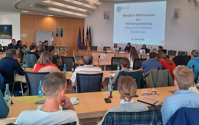 Teilnehmende der Vollversammlung des Netzwerks Teilhabe Bodensee sitzen im Sitzungssaal des Landratsamts Bodenseekreis in Friedrichshafen und verfolgen eine Präsentation zum Thema Fachkräftemangel und Teilhabe.