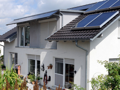 Weißen Haus mit schwarzen Dachziegeln und einer Photovoltaikanlage auf dem Dach.