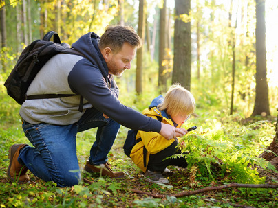 School boy and his father hiking together and exploring nature with magnifying glass. Little boy and dad spend quality family time in sunny forest of second summer. Daddy and little son